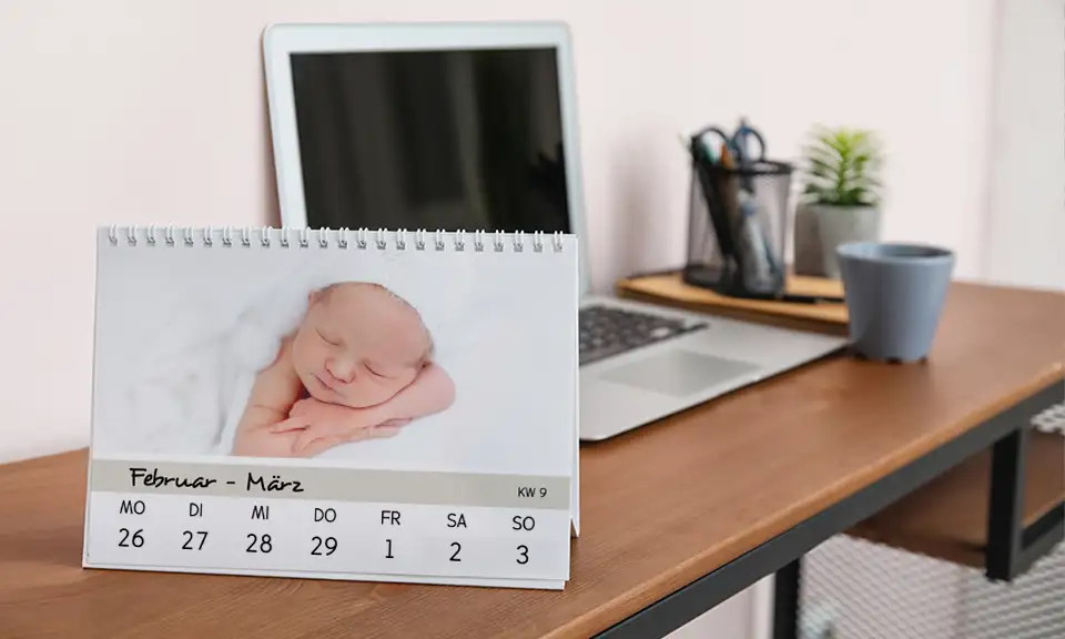 Ein Fotokalender als Tischkalender mit Fotos, der auf einem Schreibtisch vor einem Laptop steht