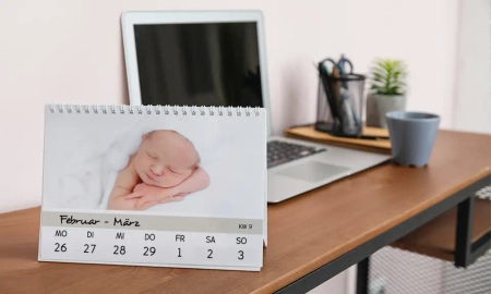 Ein Fotokalender als Tischkalender mit Fotos, der auf einem Schreibtisch vor einem Laptop steht