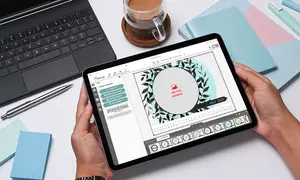 Fotokalender gestalten mit einem Tablet, daneben geöffnetes Laptop und Tasse Tee