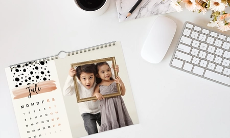 Monatskalender als Wandkalender auf Schreibtisch, daneben Tastatur und Kaffeetasse