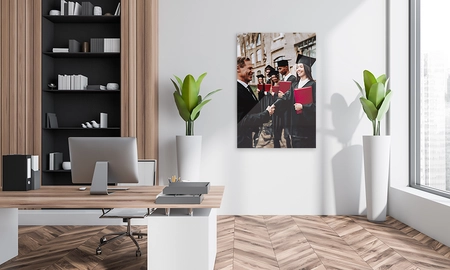 Schreibtisch mit Pflanze, im Hintergrund Alu dibond Direktdruck Wandbild mit College Absolventen