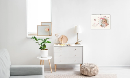 Monatskalender als Wandkalender an Wand aufgehangen, weiße Kommode mit Accessoires darunter