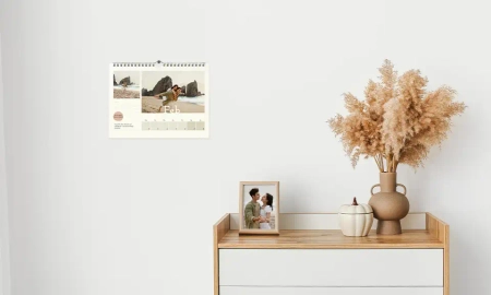 Ein Fotokalender als Wandkalender hängt neben einem Schreibtisch, auf dem Fotos stehen
