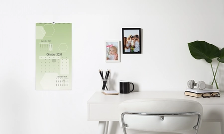 Eine Wand mit Wandkalender und gerahmten Fotos. Das Kalendarium ist grün